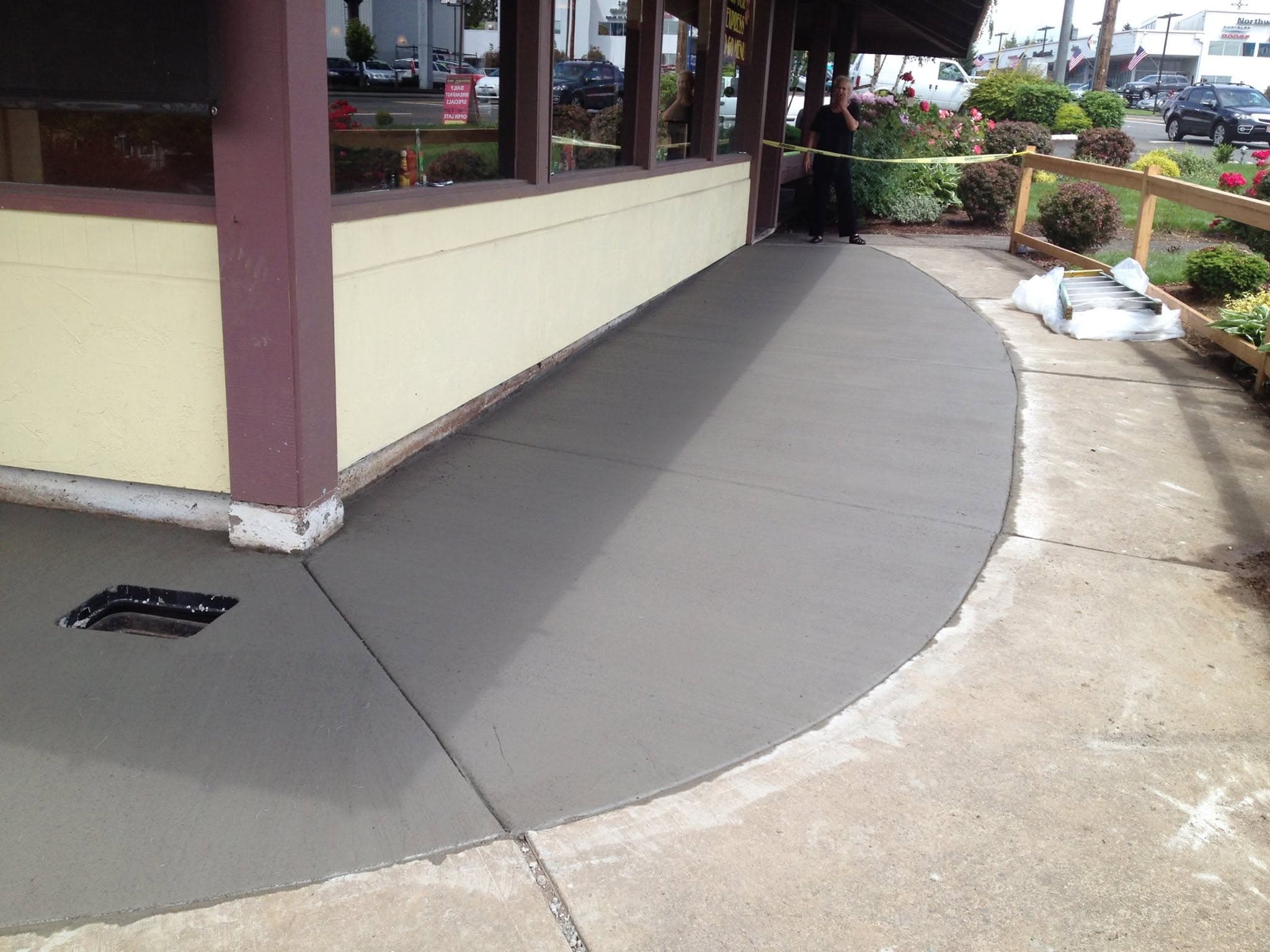 New curved concrete walkway along a restaurant's covered entrance, caution tape strung along the railing