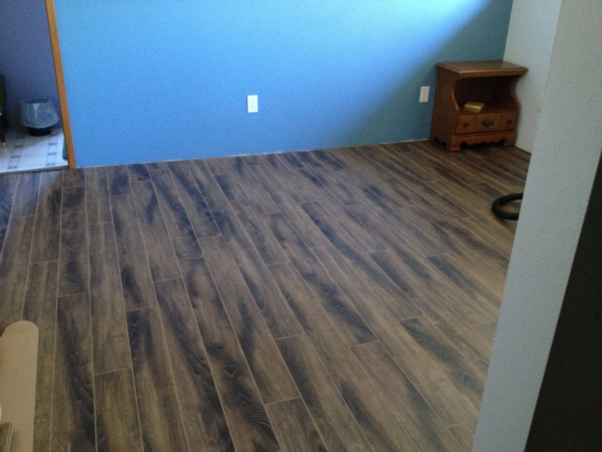 New dark wood-look laminate plank flooring in a room with a blue wall and a wooden nightstand