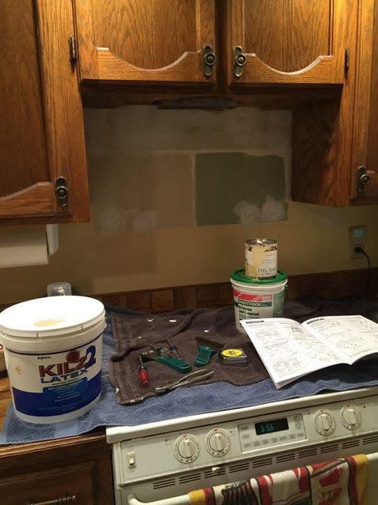 Pared de la cocina debajo de gabinetes de roble con el microondas quitado, resanada y con primer, con material de pintura sobre la estufa