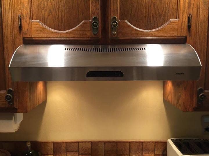New stainless steel range hood installed under oak cabinets, angled view with under-cabinet lights on