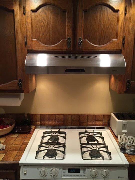 New stainless steel range hood installed above a white gas cooktop, straight-on view