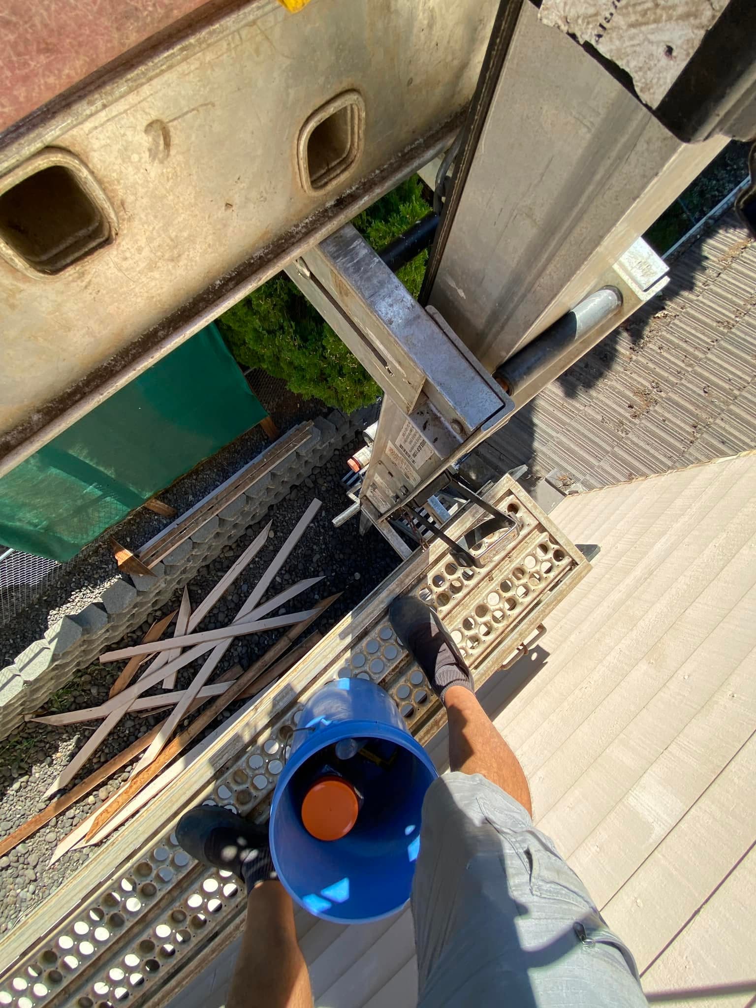 Vista hacia abajo desde una escalera de barandales de andamio, un balde de pintura y tejas del techo abajo