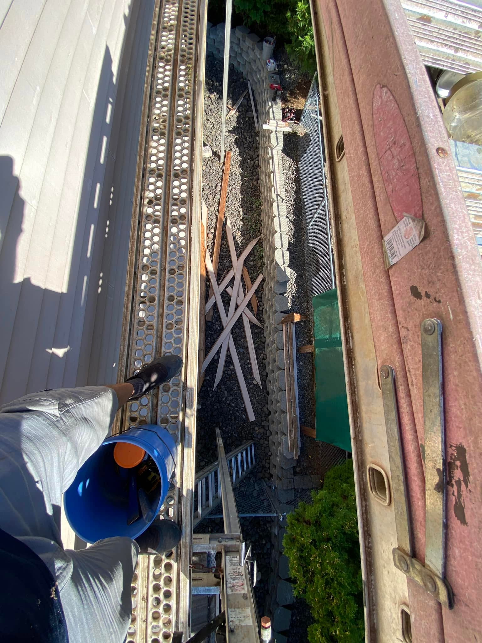 View down a ladder at scrap wood, a gravel bed, and a chain-link fence below