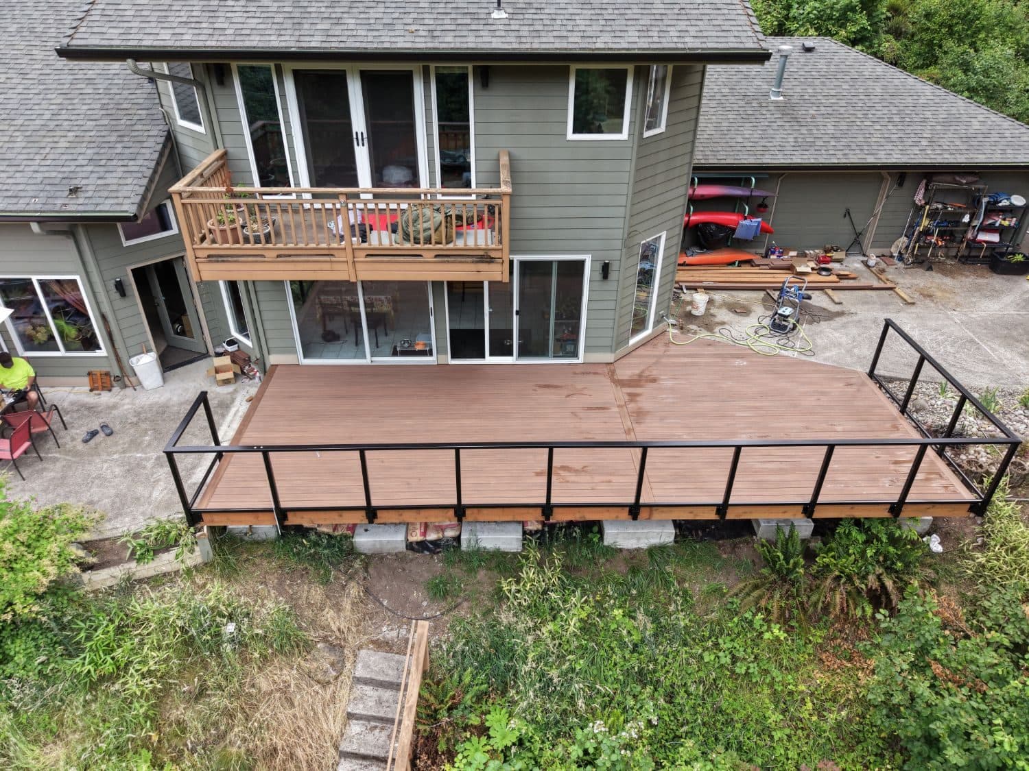 Aerial view of a large new brown composite deck with black metal railing behind a green two-story home