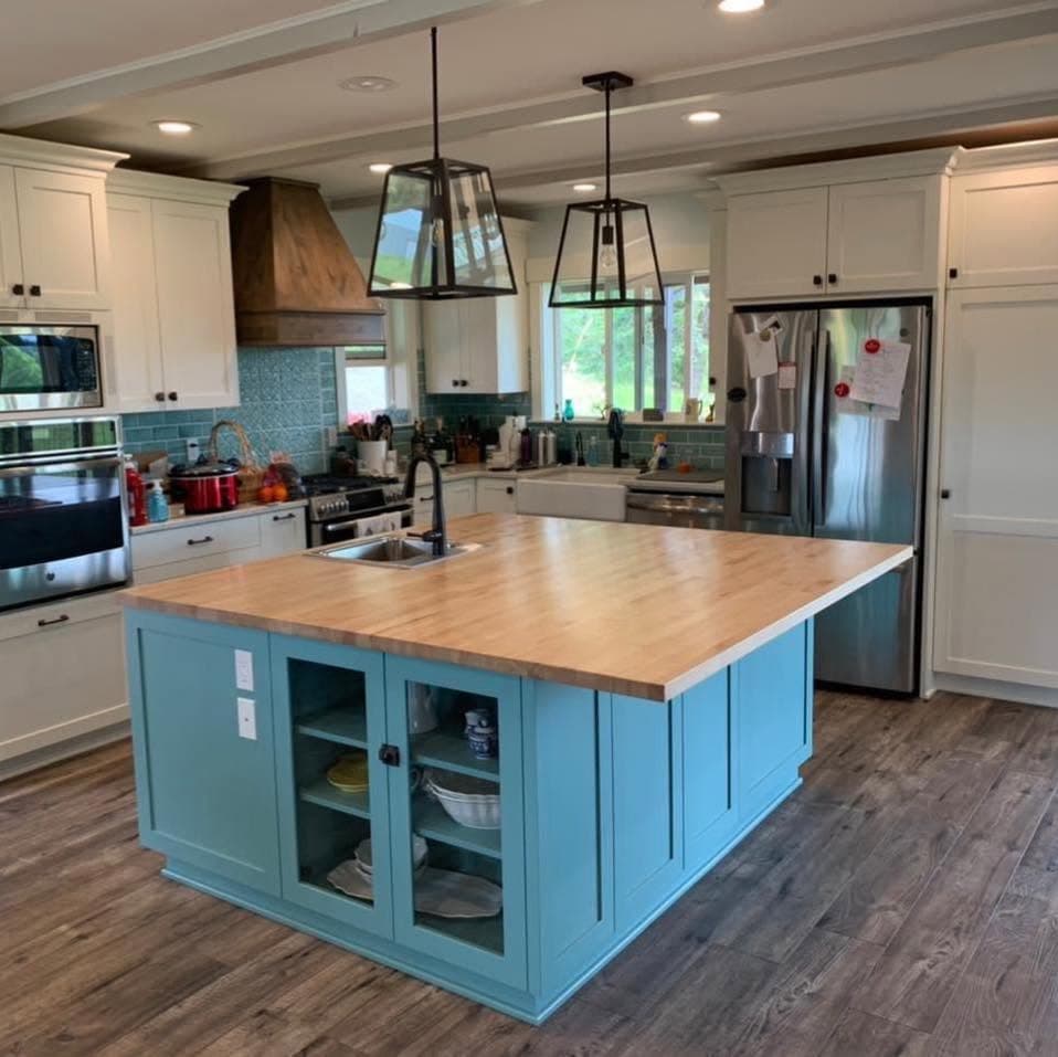 Remodeled kitchen with white shaker cabinets, teal island, tile backsplash, and stainless appliances