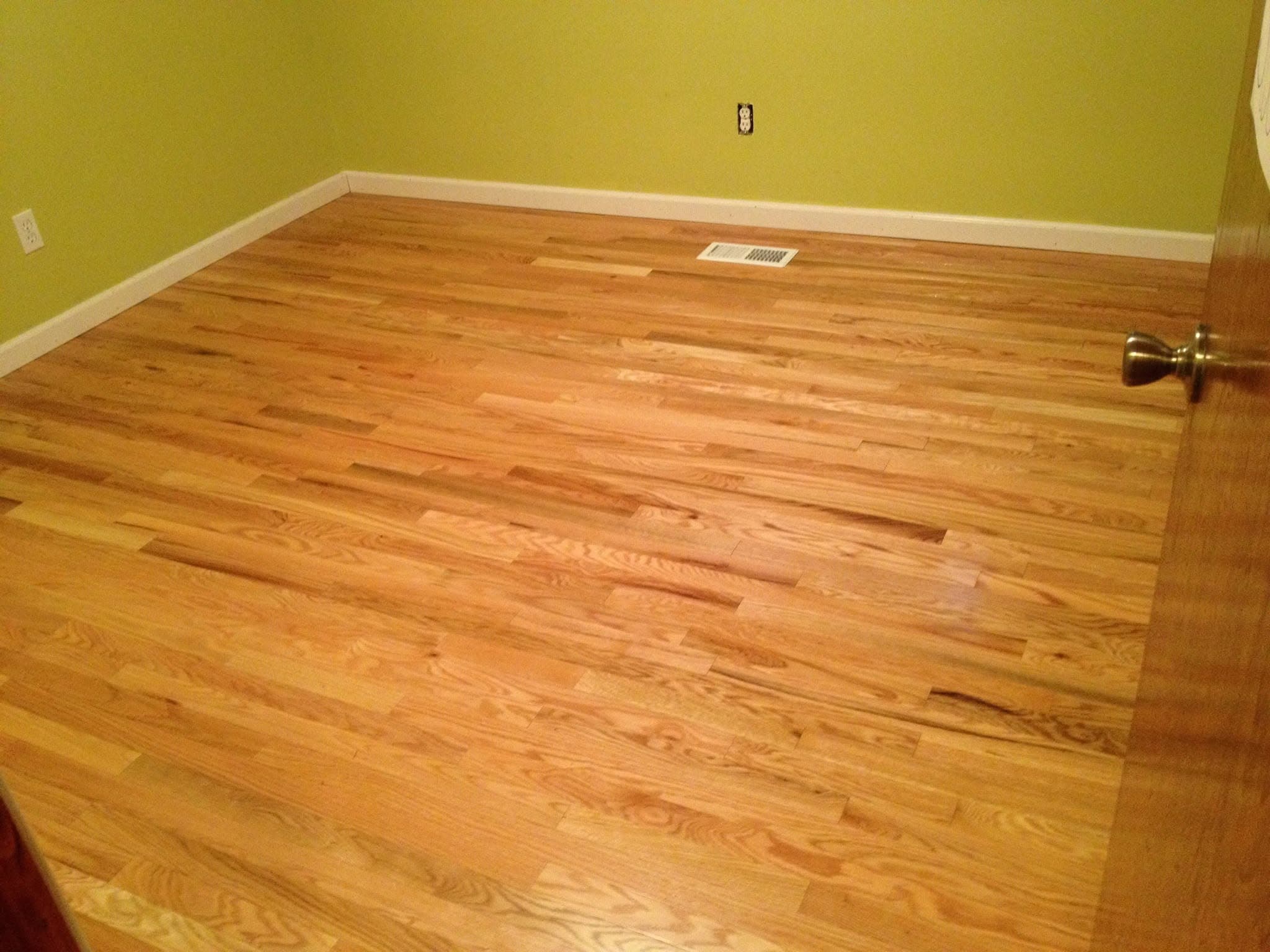 Piso de madera restaurado en un cuarto vacío con paredes verde olivo y una rejilla de ventilación en el piso